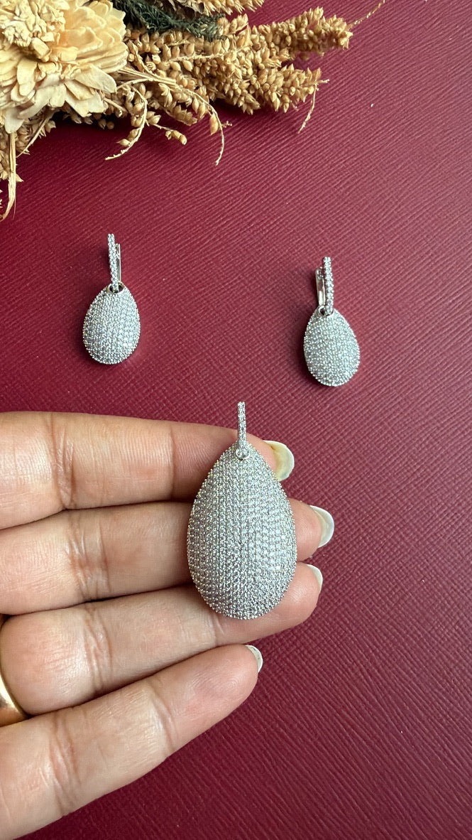 Nina American Diamond pavé teardrop pendant held in hand to show its size, with earrings above