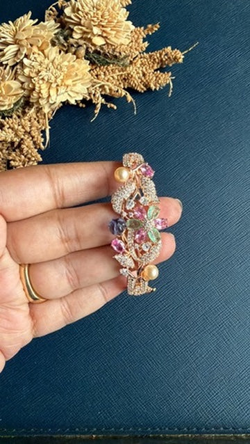 Chellan rose gold floral bracelet held in hand: pink, mint-green and purple stones with white American Diamond leaves and pearl-look beads