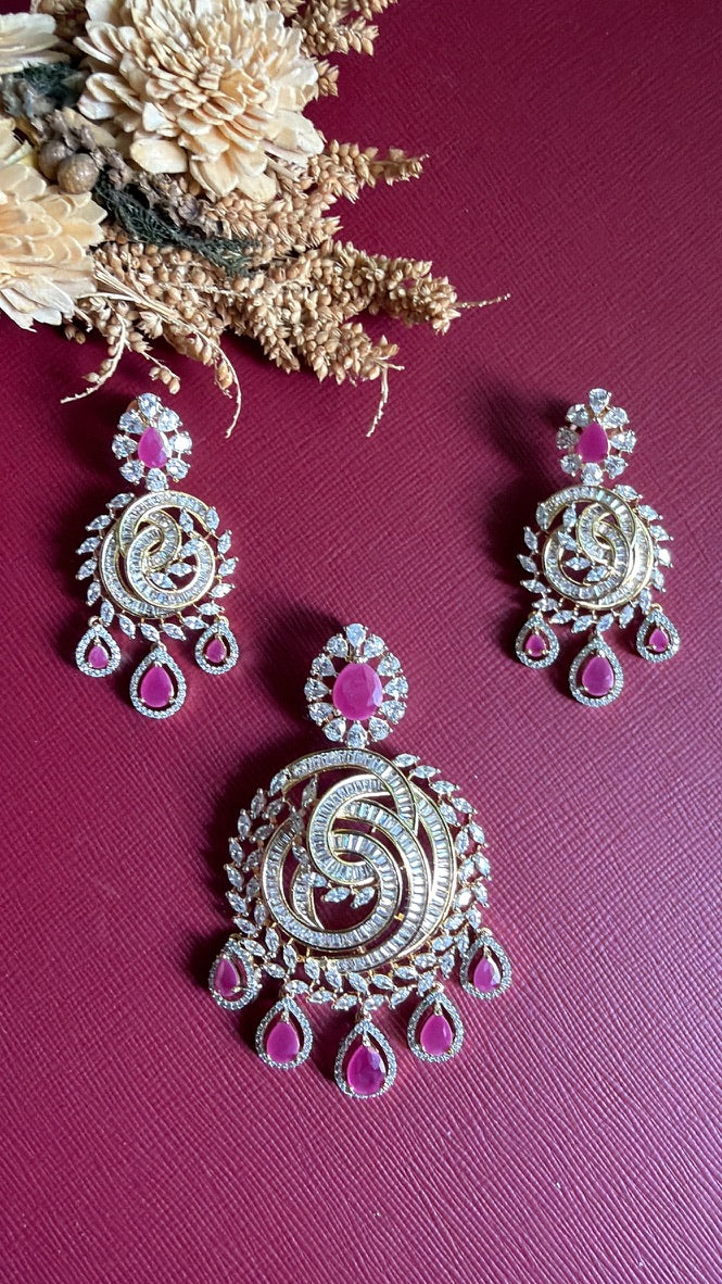Ramya pendant and earrings laid flat, five ruby-pink pear drops below a baguette-cut swirl