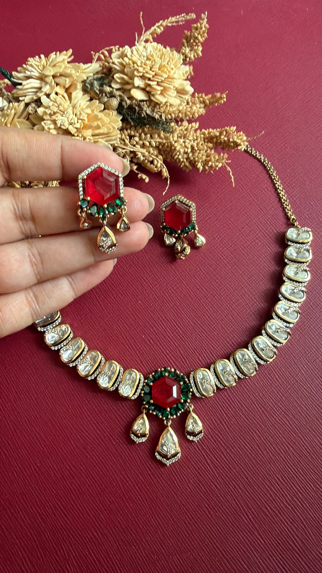 Hansika Victorian Kundan earring held in hand: hexagonal ruby-red stone ringed in emerald green with Kundan drops, beside the necklace
