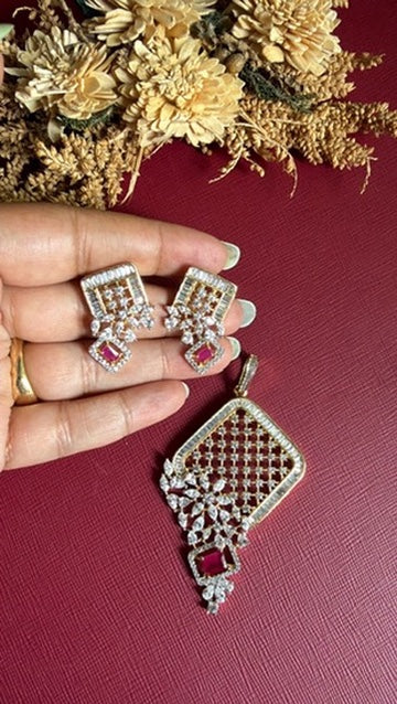 Clara dual-tone lattice pendant with white American Diamond flower spray and ruby-pink stone, with matching earrings held in hand