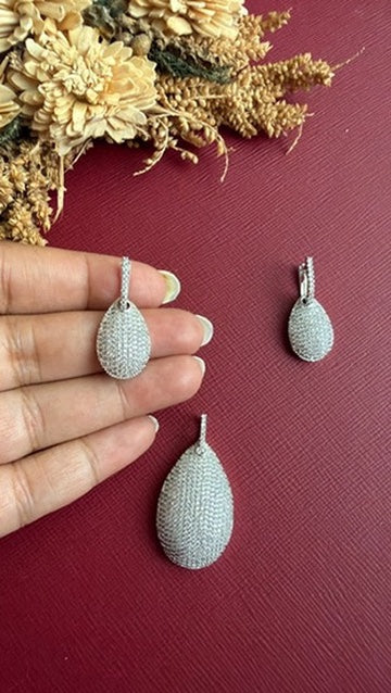 Nina pavé teardrop earring held in hand to show its size, beside the matching pendant