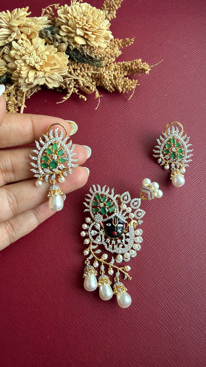 Krishika Shrinathji pendant with emerald-green coloured stones, peacock and pearl-look drops, with matching earring held in hand