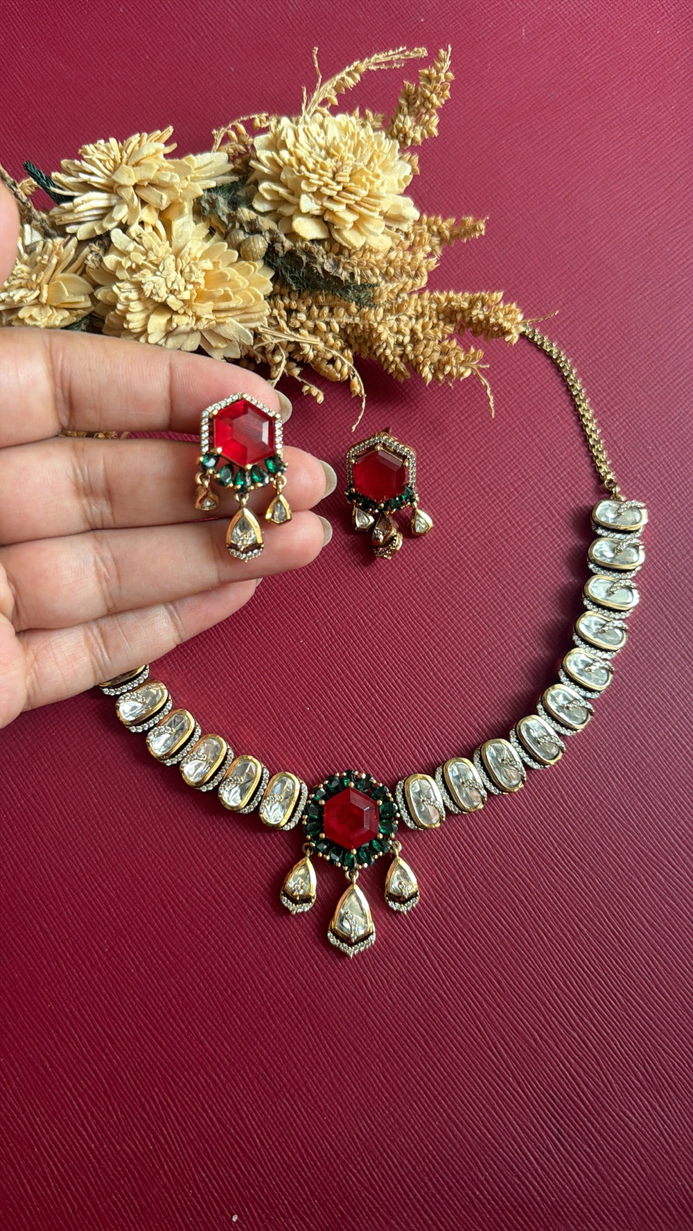 Hansika Kundan necklace with white oval Kundan stones, ruby-red and emerald-green centre and three Kundan drops, with matching earring held in hand