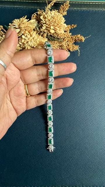 Rubina tennis bracelet held in hand, showing the full line of green stones and round CZ halos