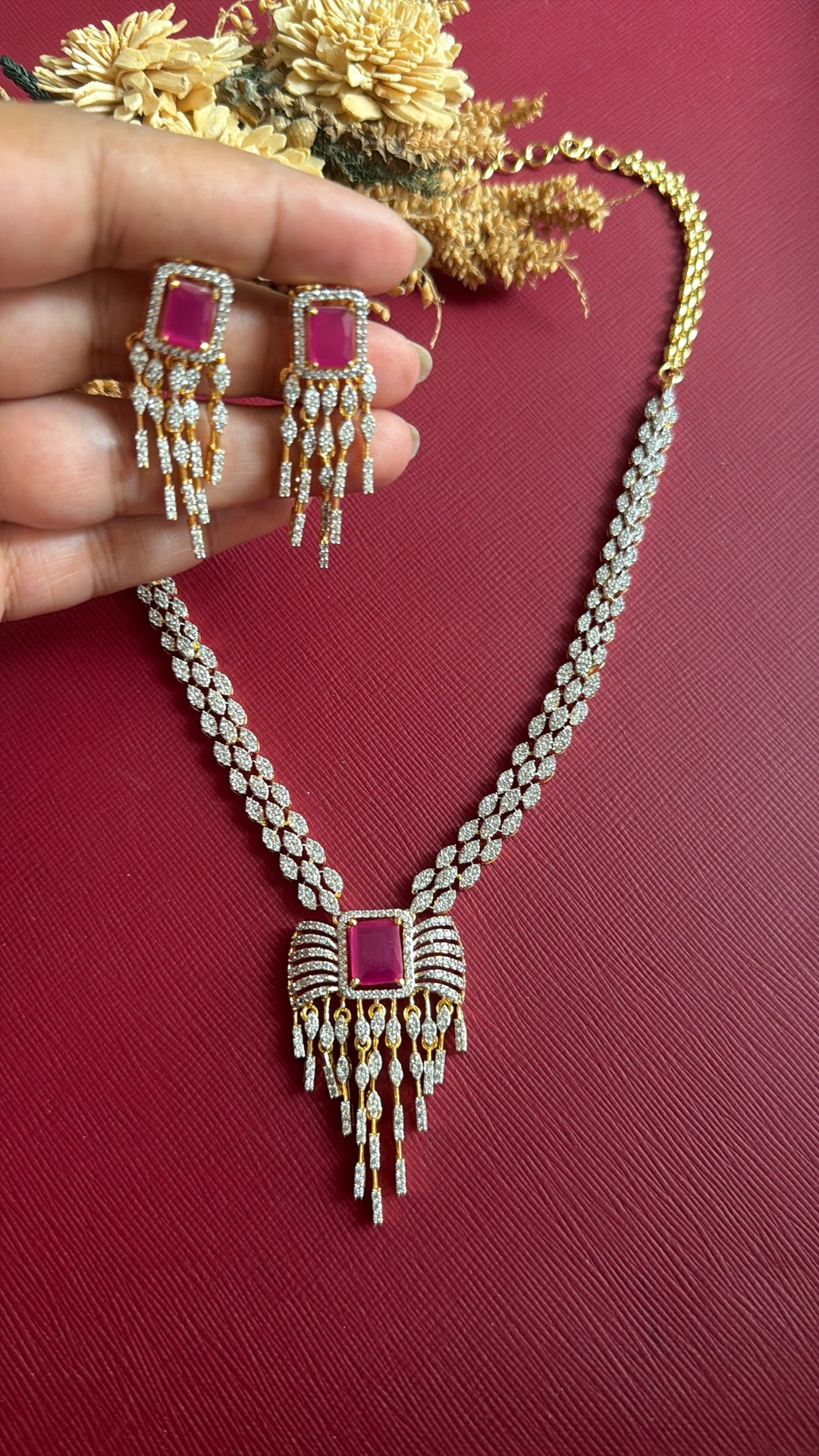 Khurmi ruby-pink American Diamond fringe earrings held in hand with matching necklace