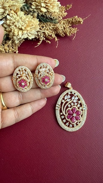 Mishka ruby-pink flower studs held in hand, with the matching oval openwork pendant beside them
