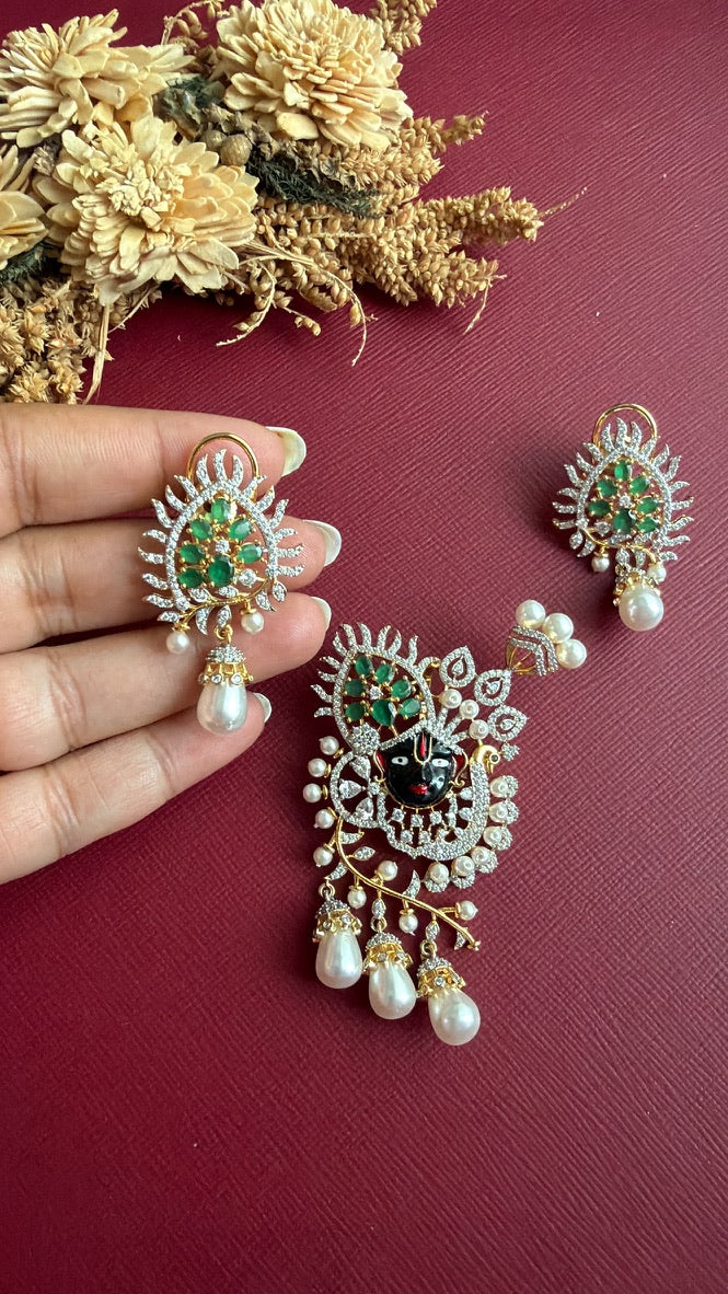 Krishika earring held in hand to show its size: green and white stone crown with a pearl-look drop and back clip, beside the Shrinathji pendant