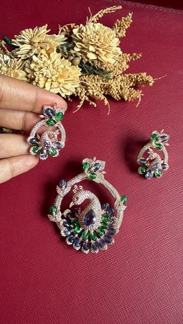 Peacock motif AD pendant and push-back earrings held in hand, blue-violet and green stones