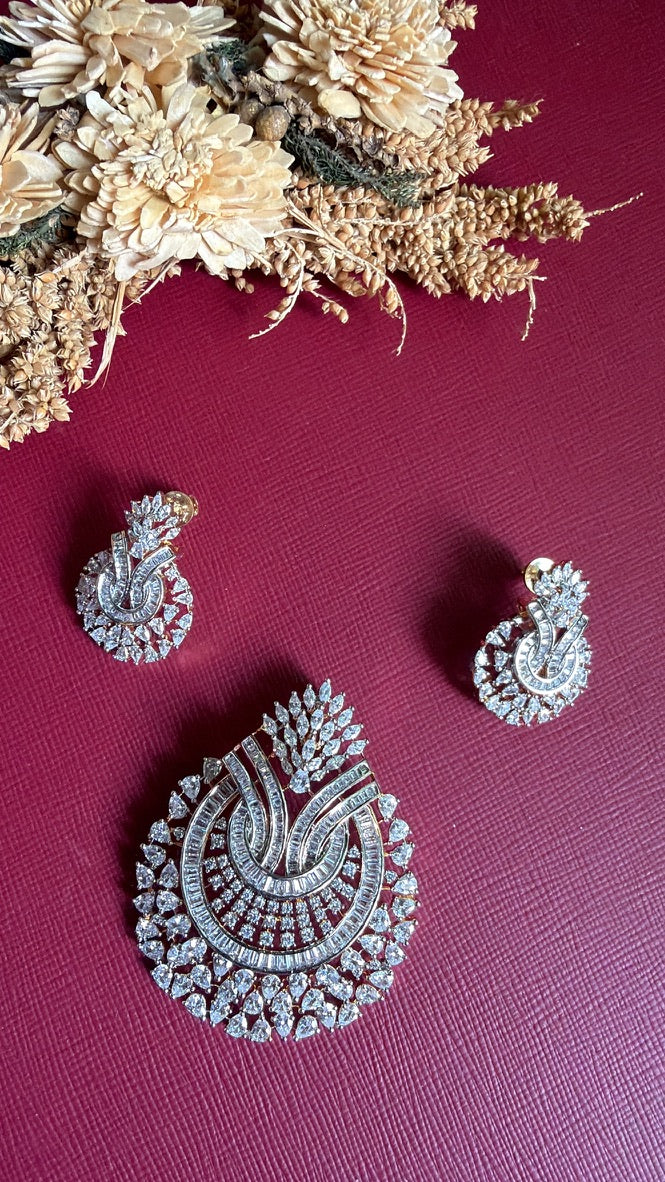 Needhi American Diamond pendant set with matching earrings: white baguette and pear-cut CZ stones on a gold-toned setting, on a maroon background