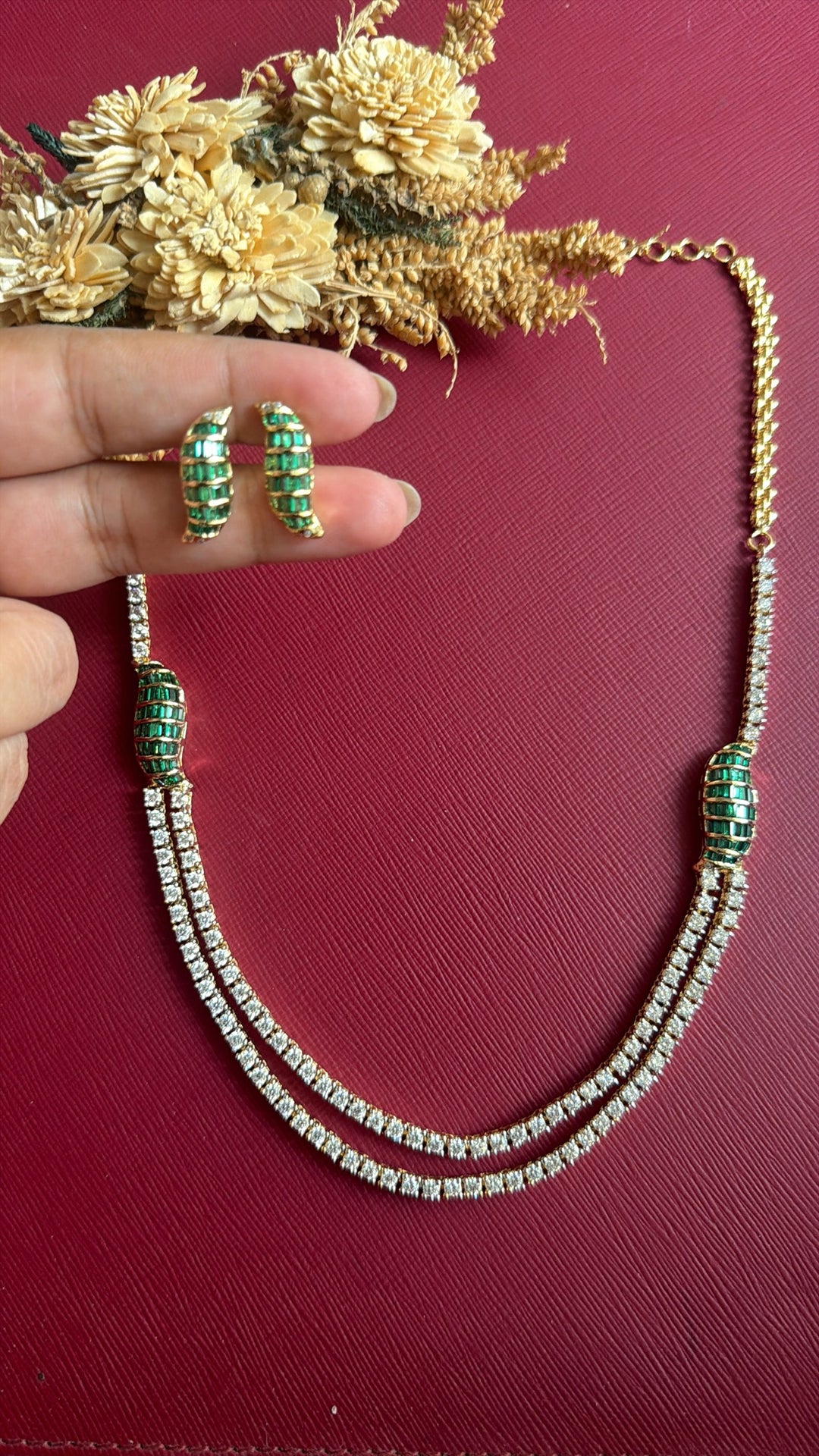 Eliana green baguette stud earrings held in hand with matching layered necklace