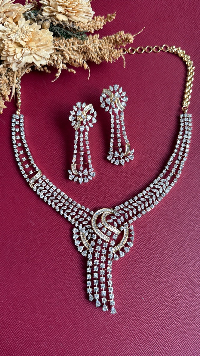 Hand holding Farida AD drop earring beside matching necklace, showing earring length and stone detail