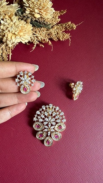 Kanika flower-burst pendant in white American Diamond with ruby-pink pear stones in baguette-framed loops, with matching earring held in hand