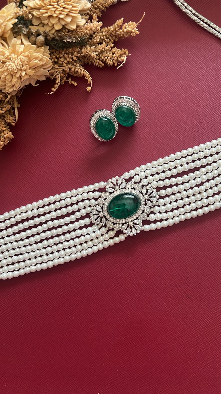 Pearl necklace with green gemstones and matching earrings on a red surface