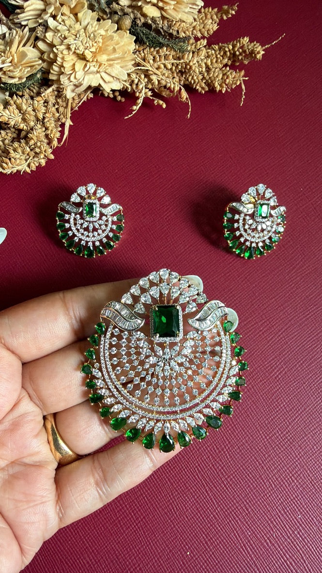 Rushika Green pendant held in hand to show its size, with the matching earrings beside it
